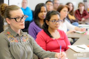 Students sitting in class paying attention to the instructor, focus is on students' faces.